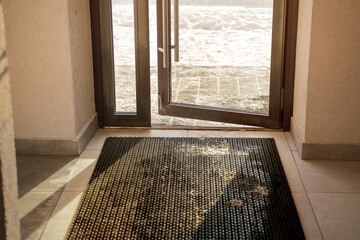 Muddy rubber doormat mounted on tiled floor inside of house entrance in winter time. Cleaning...