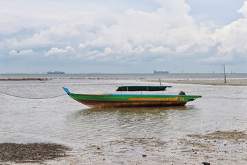 Obraz premium Small green river wooden motor boat for fishing and transporting tied up at the shallow sea.