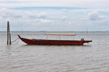 Small long brown river wooden motor boat for fishing and transporting tied up at the shallow sea. - Powered by Adobe