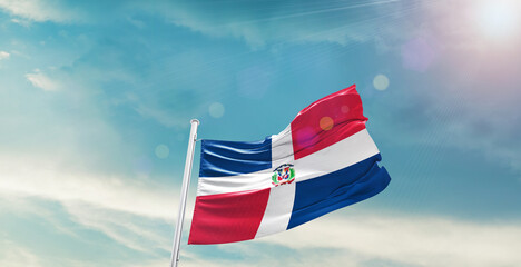 waving flag of Dominican Republic in blue sky. the symbol of the state on wavy cotton fabric.