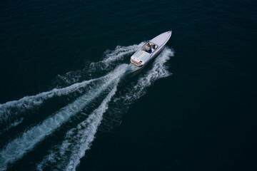 Speedboat with a man moving diagonally. White boat fast movement on dark water, white trail on the water.