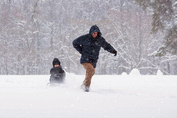 Father and son are walking in Tsaritsyno Park in a heavy snowfall. A father pulls his little son on a sled in a winter park.