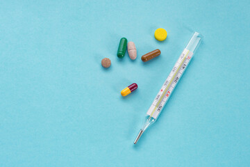 Mercury thermometer and tablets on a blue background. Concept of pharmaceuticals, medicines. Thermometer and multicolored pills, top view. Minimal creative concept. Copy space. 