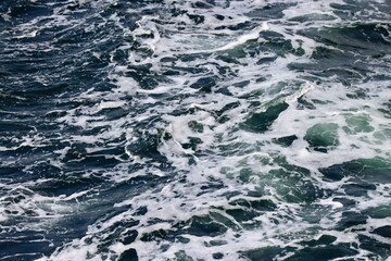 Stern waves with white foam tips on greyish blue sea water, photo taken from aboard ship. Selective focus