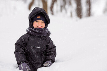 Portrait of a beautiful little Russian boy in winter in the park. Snow is falling. Cold. Red...