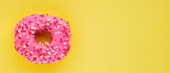 Strawberry donut with pink icing and sprinkles. Sweet pink donut on yellow background. Flat lay. Copy space