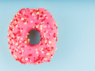 Donut with icing on pastel blue background. Pink donut with colorful toppings. Copy space