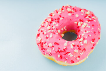 Donut with icing on pastel blue background. Pink donut with colorful toppings. Copy space