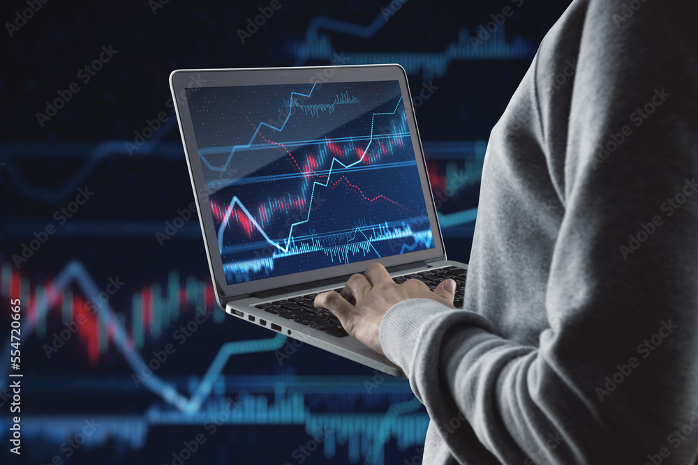 Poster Close up of hand holding and using laptop with glowing forex index chart/graph on dark background. Trade, finance and fintech concept.