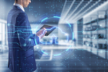 Young european businessman using tablet with glowing cloud hologram on blurry office interior background. Server and data storage concept. Double exposure.