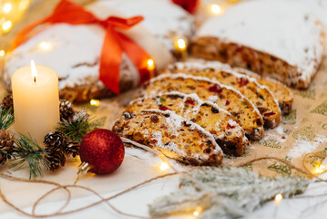 Traditional German Christmas stollen made of dried fruits and nuts, sprinkled with powdered sugar on the background of a Christmas decor with candles. A festive treat.