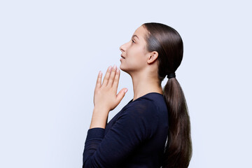 Young female pleading, holding hands in prayer on white background, profile view