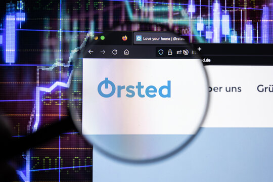 Orsted company logo on a website with blurry stock market developments in the background, seen on a computer screen through a magnifying glass