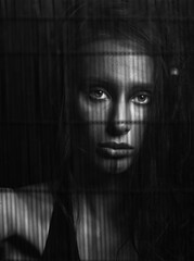 Fashion and make-up concept. Beautiful woman portrait. Model with dreadlocks and make-up looking at camera through wooden black grated wall with white eyes. Black and white image