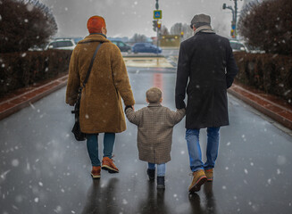 dad, mom and child are walking under the snow