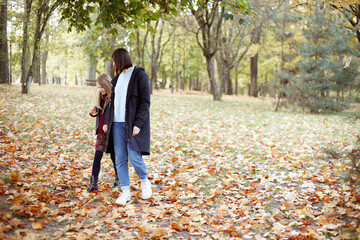 Merry, smiling family of mother and daughter strolling around in autumn forest. Travelling and have fun in countryside