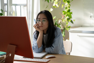 Young serious Asian girl student watching webinar video course on desktop computer while studying...