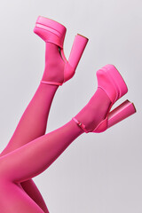 Unknown glamous woman dressed in pink tights and high heeled shoes isolated over grey background. Female feet in fashionable sandals holding up in air. Fashion and style concept. Slender legs