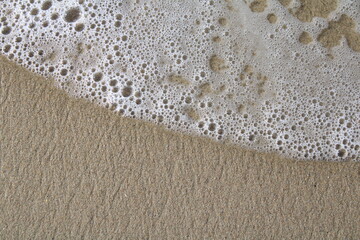 Fototapeta na wymiar Wave Washing ashore on beach with small bubbles