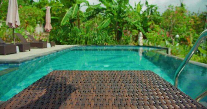 Woman hand brings a cup of hot balinese coffee to the pool with beautiful blurred nature landscape background, slow motion.