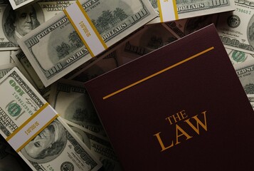 Law textbook on the background of scattered dollars, banknotes. The concept of making money in law,...