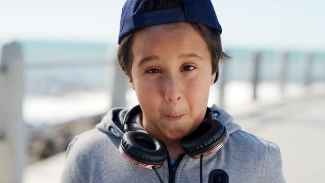 Comic face, playful and child by sea, happy music and silly expression on the promenade in the Philippines. Travel, holiday and portrait of a crazy boy kid being funny at the ocean with headphones