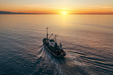 Fishing boat catching fish at sunset aerial view from drone. Small fishing trawler ship on sea...