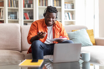 Cheerful african american man student attending webinar, using laptop