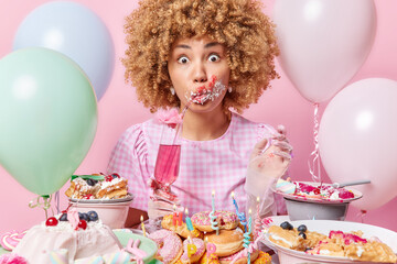 Surprised displeased curly haired woman drinks pink cocktail from straw smeared with cream around...