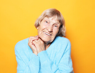 Cheerful old lady in a blue sweater laughs and rejoices on a yellow background.