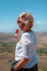 Portrait: attractive adult young blonde woman in sunglasses turned back and looks at the camera...