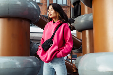 Beautiful stylish Asian young woman in pink sweatshirt and jeans posing while looking at the...