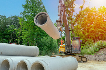 Big diameter concrete pipes for drainage works delivered on construction site and offloaded by excavator - obrazy, fototapety, plakaty