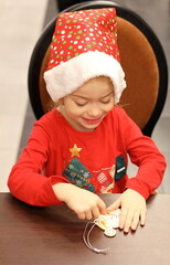 A small child is coloring a Christmas decoration with crayons. Christmas clothes and santa hat.