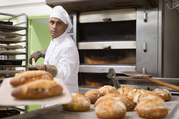 Baker taking out from oven baked bread, industrial bread production