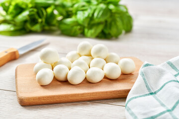 mini mozzarella cheese balls with fresh green basil on a kitchen table.