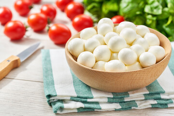 small balls of fresh white soft Italian mozzarella cheese, ripe red cherry tomatoes and fresh green basil herb, ready for making caprese salad.