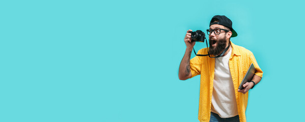 Young funny hipster photographer isolated on blue background with laptop in hand. Lifestyle work as a freelancer