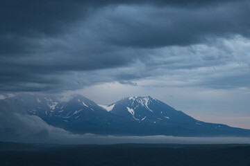 Fototapeta na wymiar Beautiful evening landscape. View of the volcanoes at dusk. Overcast weather. Low clouds. The majestic nature of the Kamchatka Peninsula. Travel and tourism in Siberia and the Russian Far East. Russia