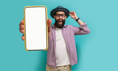 Young crazy bearded charismatic hipster showing big empty white smartphone screen for copy space and advertising area isolated on blue studio background. Mobile App Advertisement. Display Mock Up - obrazy, fototapety, plakaty