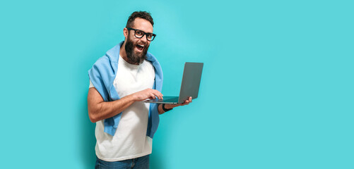 Young bearded charismatic man hipster. Shocked or surprised expression. Laptop concept. Promotion poster. Programmer, web developer holding a laptop in his hands and looking at the camera