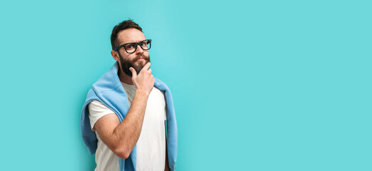 Caucasian handsome man with a beard is isolated on a blue background, he having doubts and thinking how to find a way out of the current situation. Look for an idea