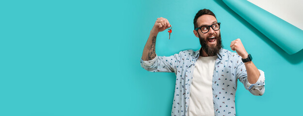 Happy guy holds the keys to his new own apartment, isolated on a blue background. The guy moved
