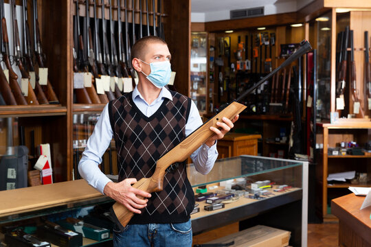 Portrait of gun store owner wearing medical face mask demonstrating modern sporting break-barrel air rifle. Concept of work and social distancing in pandemic
