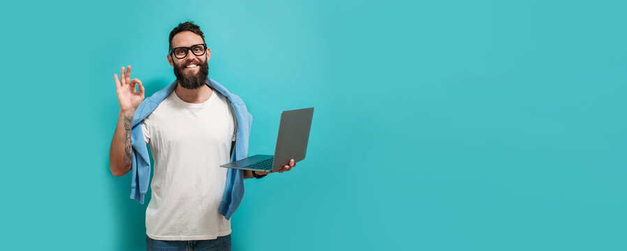 Young bearded charismatic man hipster. Shocked or surprised expression. Laptop concept. Promotion poster. Programmer, web developer holding a laptop in his hands and looking at the camera
