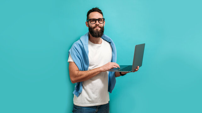 Young bearded charismatic man hipster. Shocked or surprised expression. Laptop concept. Promotion poster. Programmer, web developer holding a laptop in his hands and looking at the camera