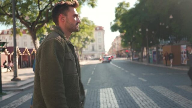 Side view confident young adult styles man in sunglasses walking city cross walk at day, crossing the street using crosswalk while looking around. Handsome guy well dressed walk european city