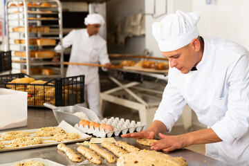 Concentrated baker preparing sweet buns in bakery kitchen