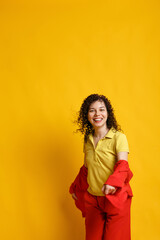 Curly cute girl laughs and jumps. Studio portrait of a woman on a bright yellow background. Happy smiling young female dancing in bright clothes