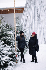 Mom and daughter choose Chritsmas tree at the fair. Girls measure fir tree using using a wooden...